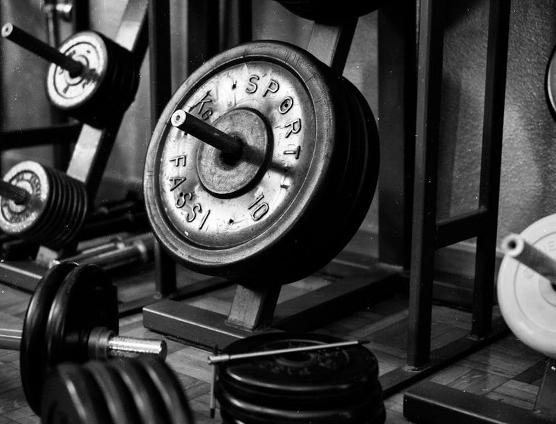 Dimly lit gym interior with heavy iron dumbbells on floor.